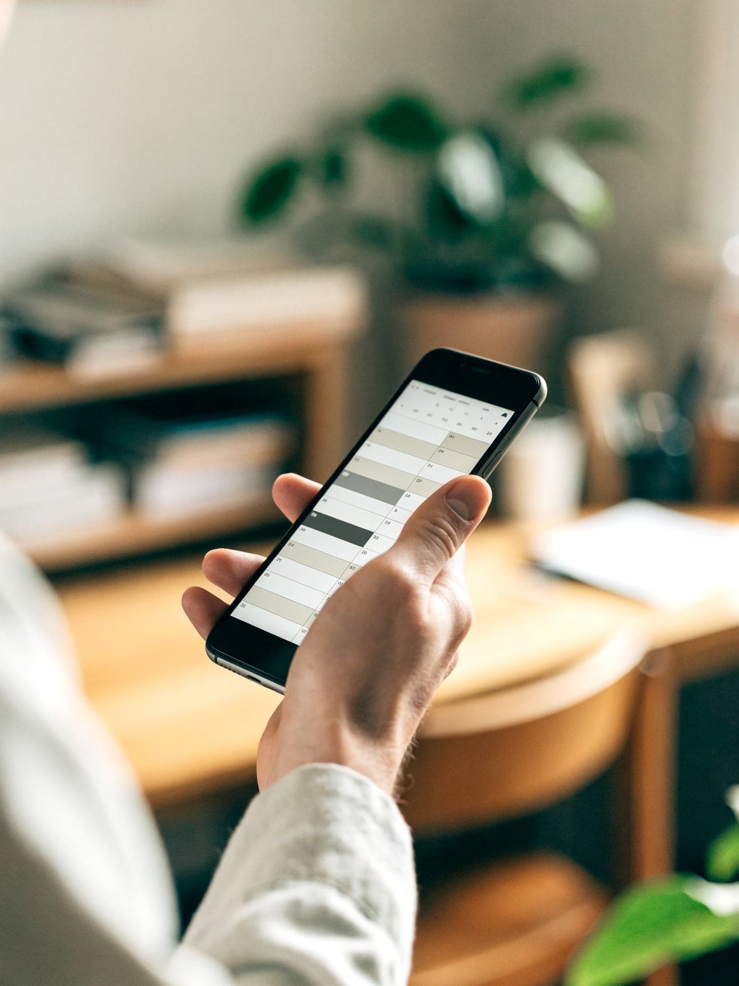 Hand hält ein Smartphone mit Terminkalender über dem Schreibtisch