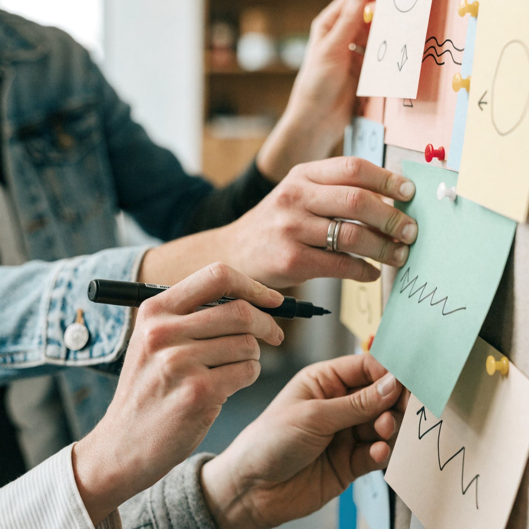 Hände ordnen im Strategie-Workshop Moderationskarten an einer Pinnwand