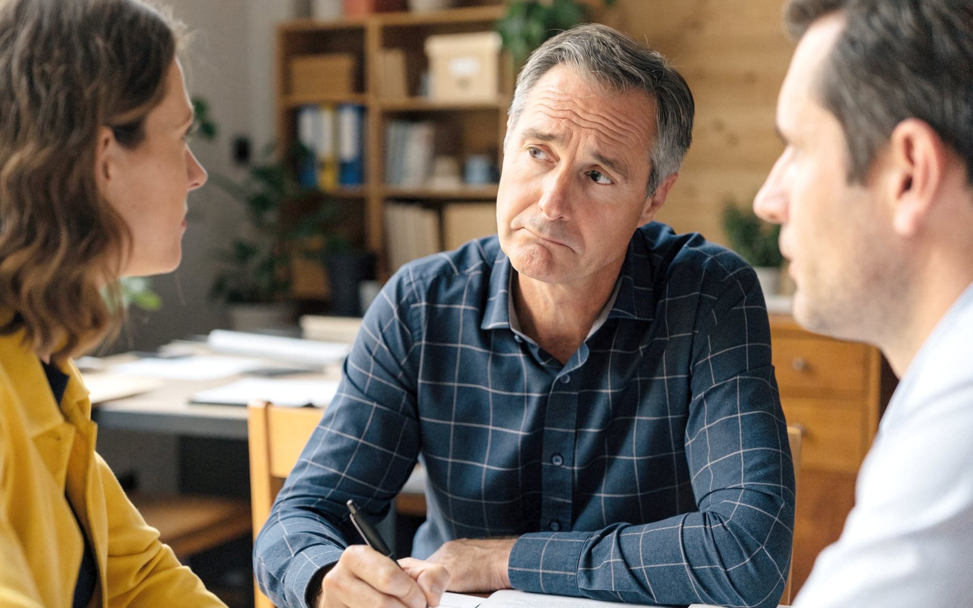 Unternehmer hört zwei Agenturvertretern skeptisch zu und schreibt mit
