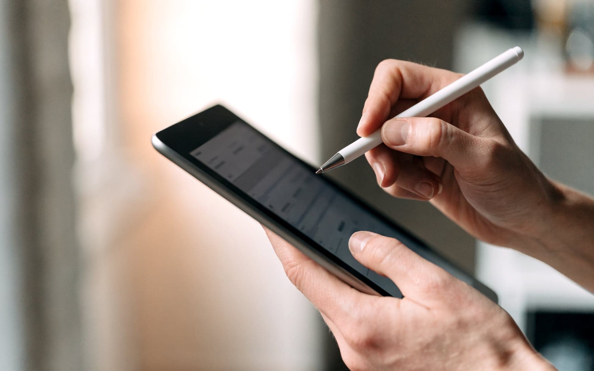 Hand füllt mit einem Stift einen kurzen Fragebogen auf dem Tablet aus