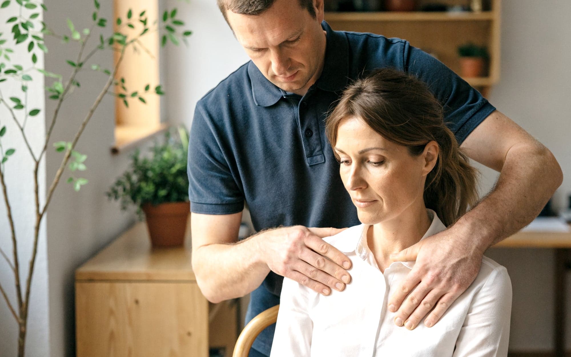 Physiotherapeut behandelt die Schulter einer Patientin in seiner Praxis