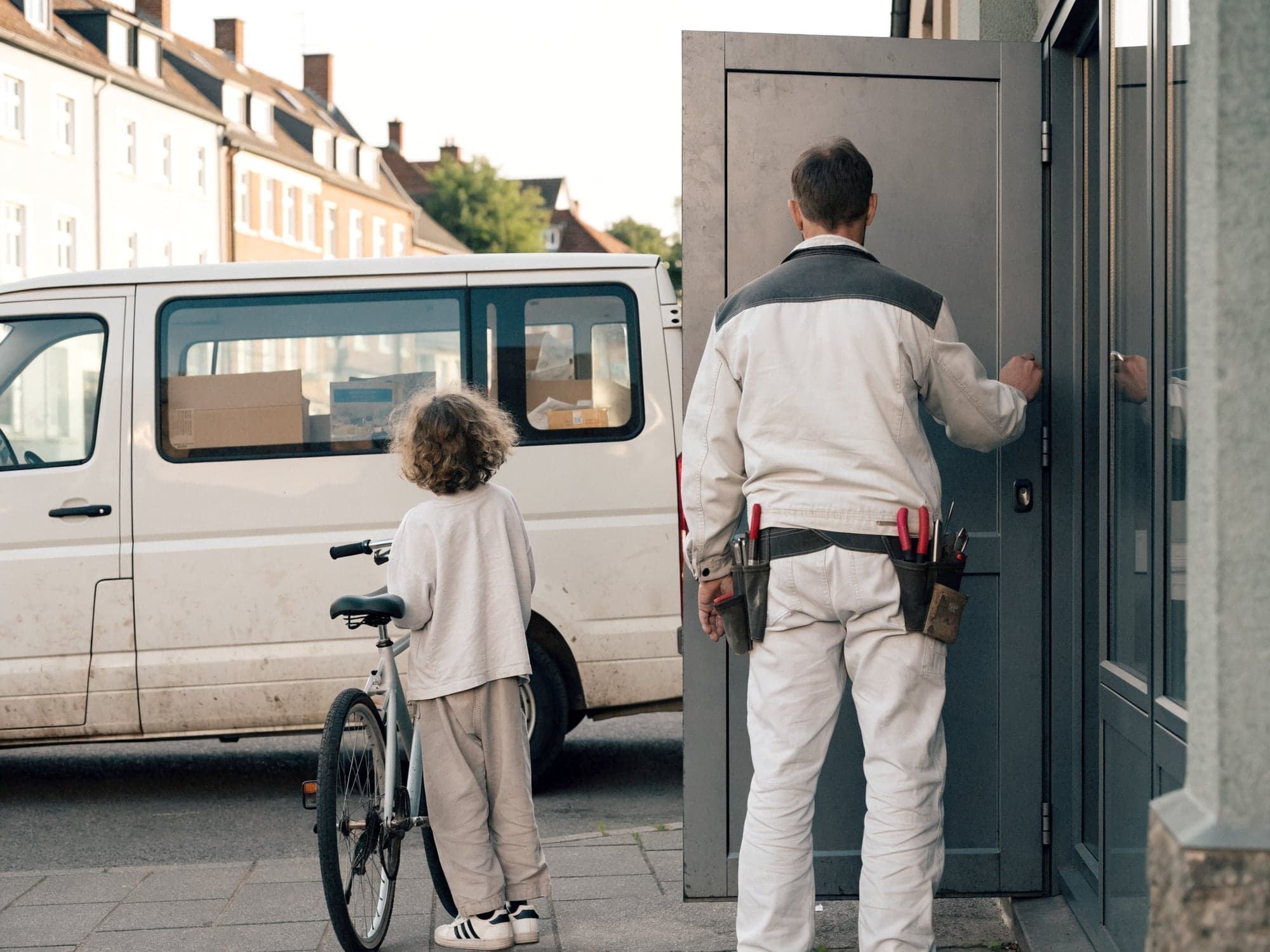 Handwerker schließt am frühen Abend die Werkstatt ab, sein Kind wartet mit dem Fahrrad